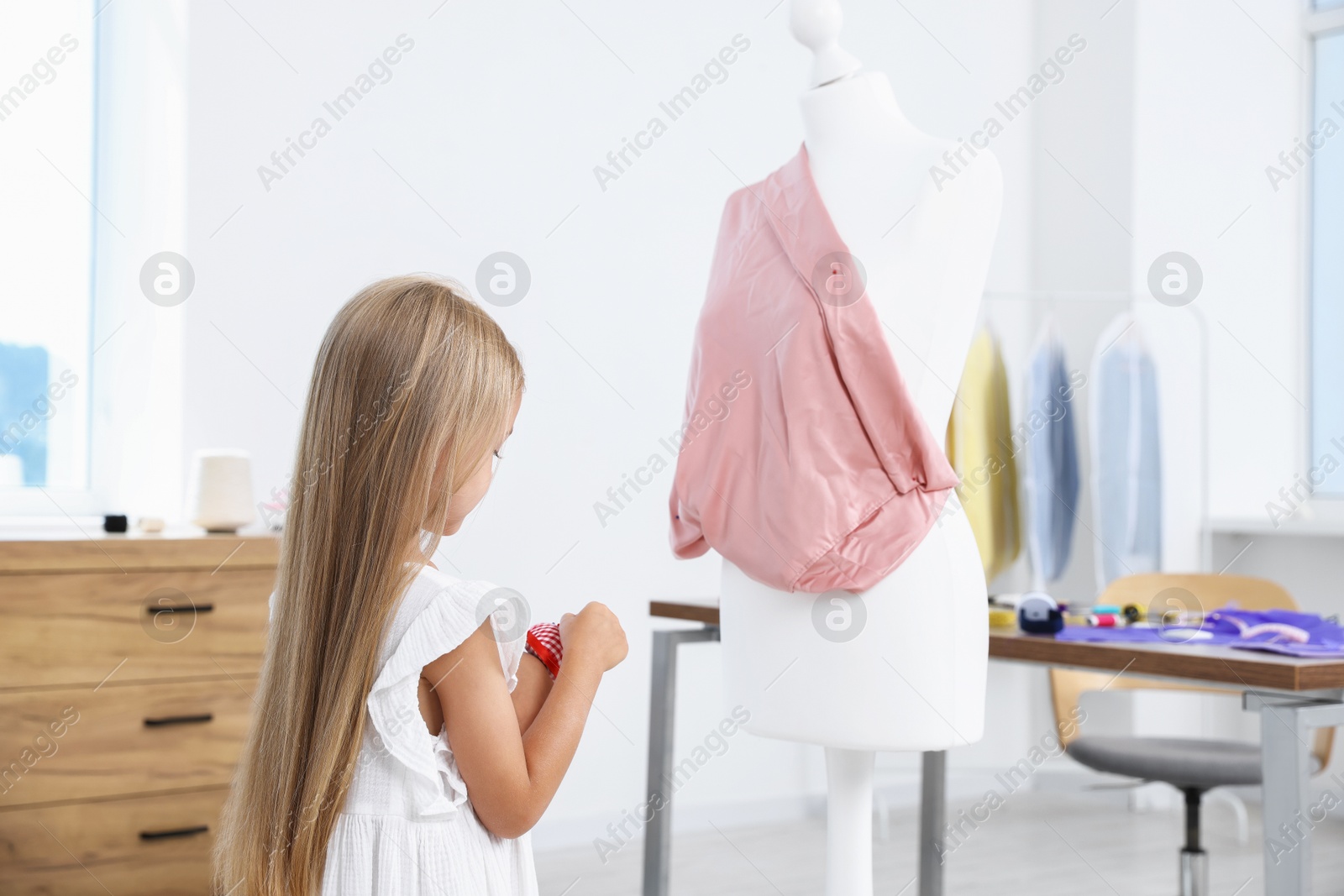 Photo of Choice of profession. Little girl with pin cushion pretending to be seamstress near mannequin in atelier