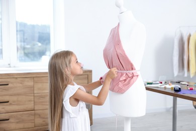 Photo of Choice of profession. Little girl with measuring tape taking measurements of cloth in atelier