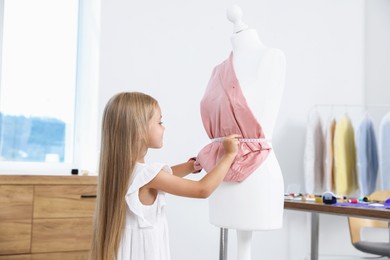 Photo of Choice of profession. Little girl with measuring tape taking measurements of cloth in atelier