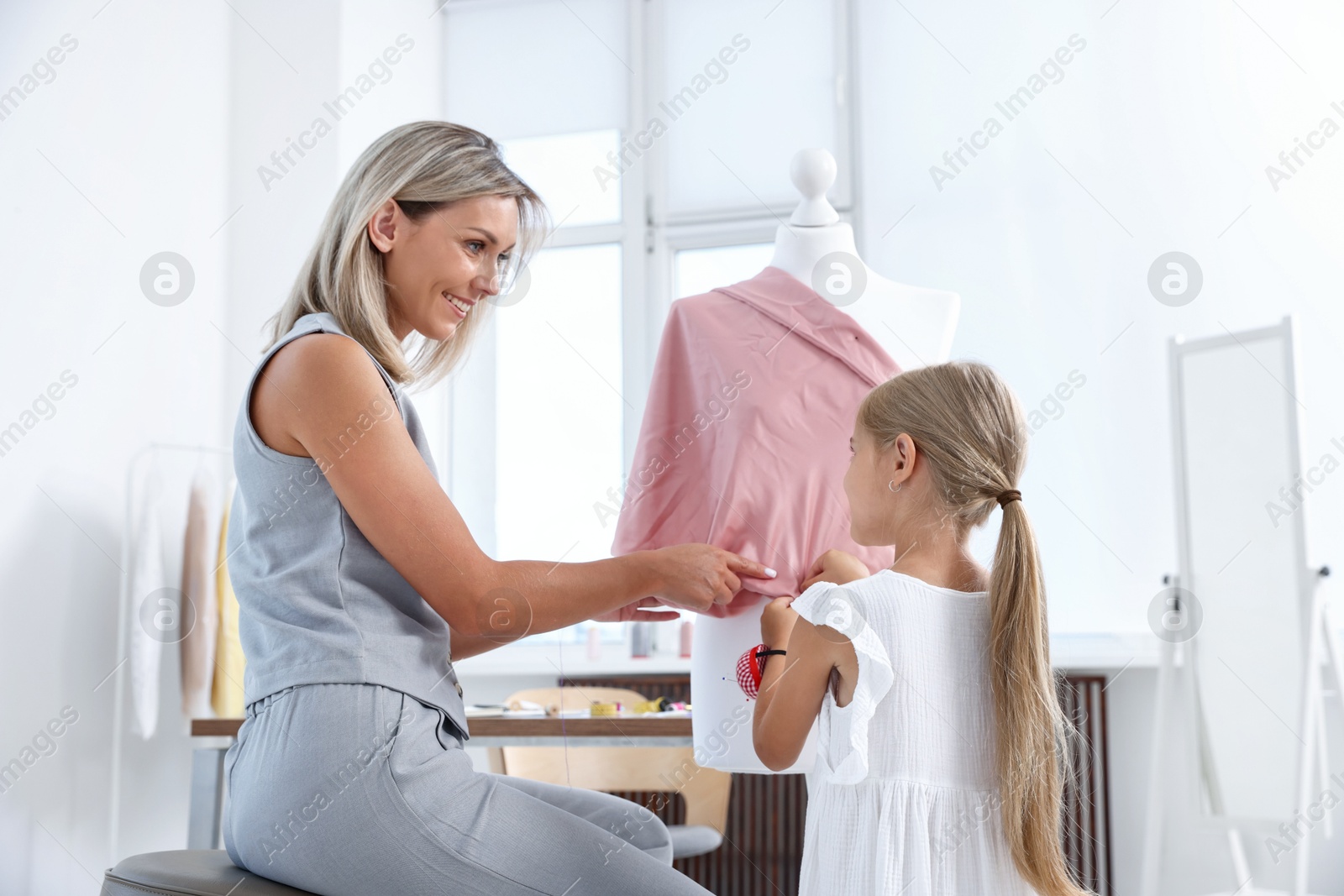 Photo of Choice of profession. Little girl helping her mother working with mannequin in atelier