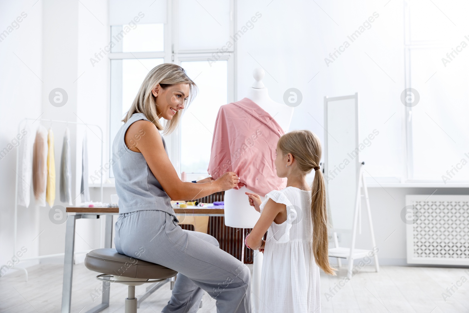 Photo of Choice of profession. Little girl helping her mother working with mannequin in atelier