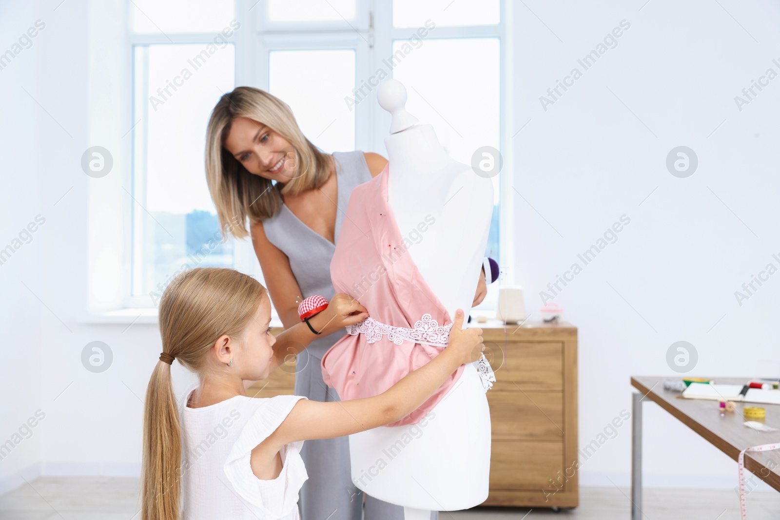 Photo of Choice of profession. Little girl helping her mother working with mannequin in atelier