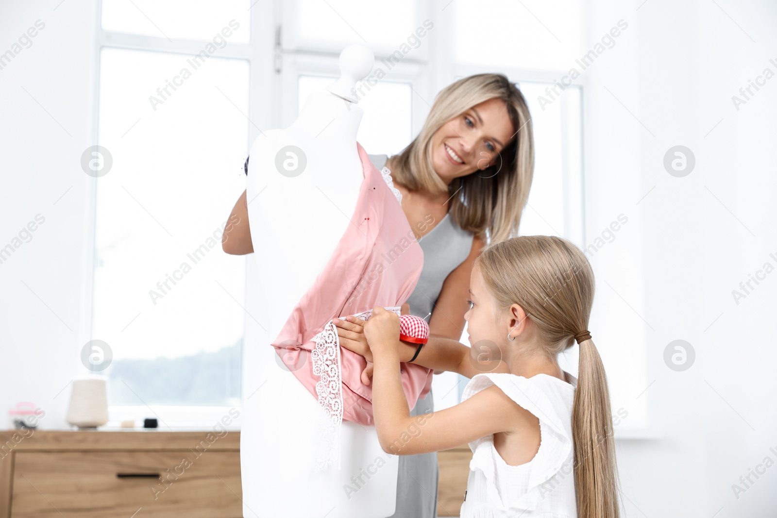 Photo of Choice of profession. Little girl helping her mother working with mannequin in atelier