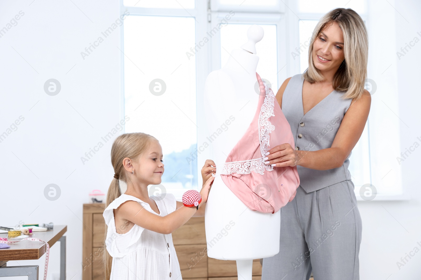 Photo of Choice of profession. Little girl helping her mother working with mannequin in atelier