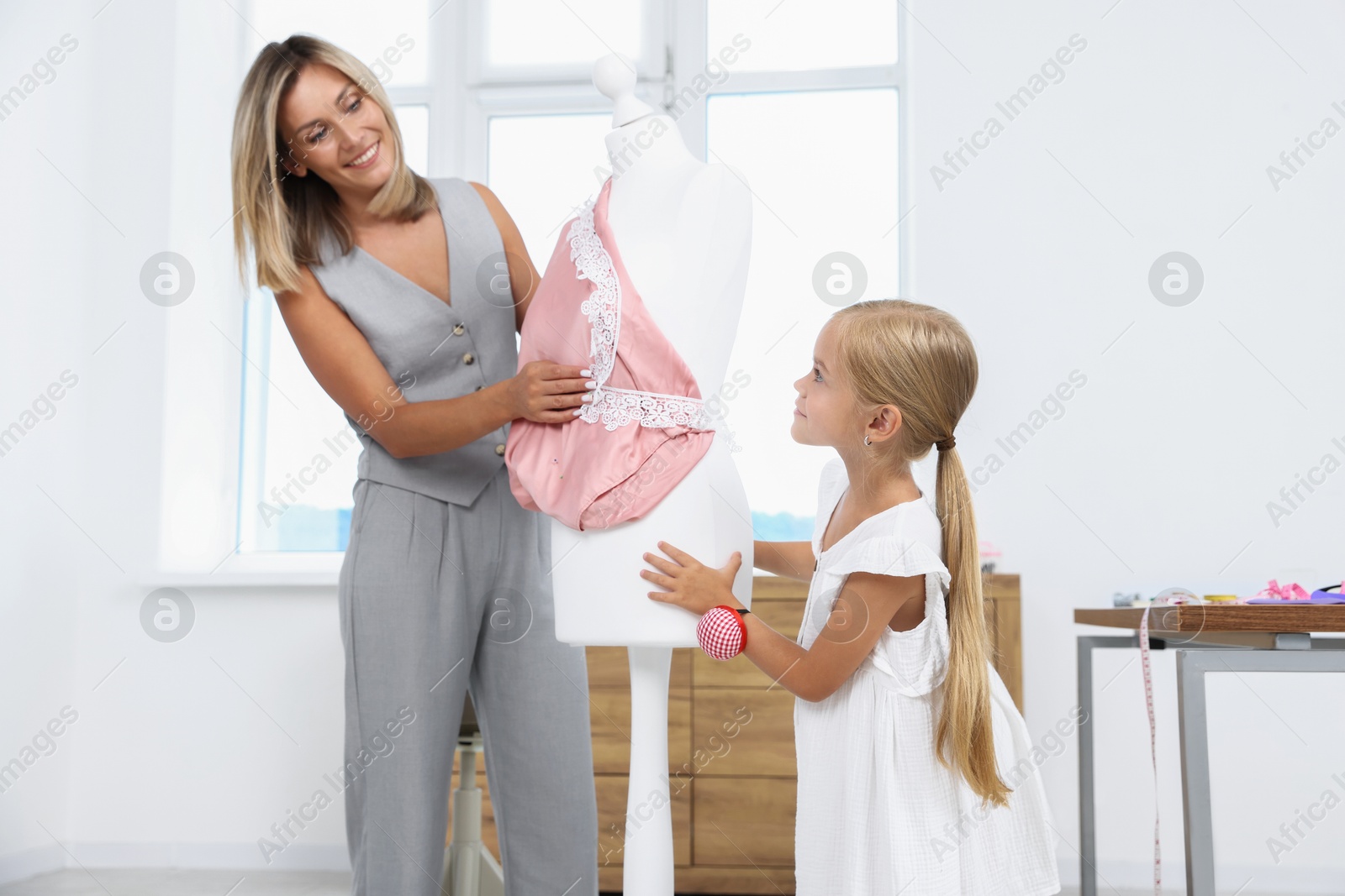 Photo of Choice of profession. Little girl helping her mother working with mannequin in atelier