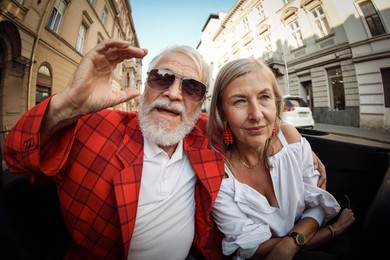 Photo of Senior couple enjoying cabriolet ride in city, wide angle lens