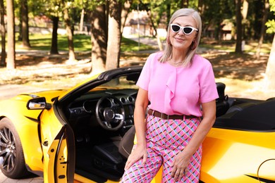 Photo of Stylish senior woman in sunglasses near modern cabriolet outdoors