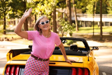 Photo of Stylish senior woman in sunglasses near modern cabriolet outdoors