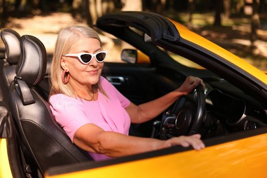 Photo of Stylish senior woman in sunglasses driving modern cabriolet outdoors