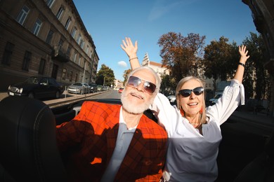 Photo of Senior couple enjoying cabriolet ride in city, wide angle lens