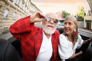 Photo of Senior couple enjoying cabriolet ride in city, wide angle lens