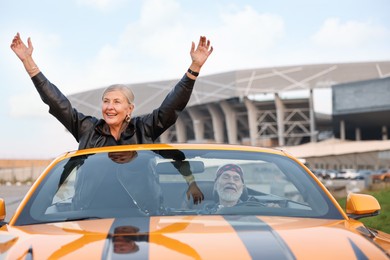 Photo of Senior couple enjoying cabriolet ride in city. Woman with wide open arms