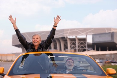 Photo of Senior couple enjoying cabriolet ride in city. Woman with wide open arms