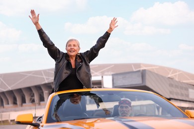 Photo of Senior couple enjoying cabriolet ride in city. Woman with wide open arms