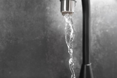 Photo of Water dripping down from faucet on grey background, closeup. Space for text