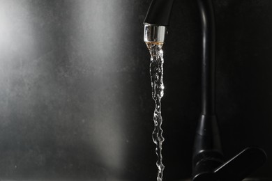 Photo of Water dripping down from faucet on grey background, closeup. Space for text