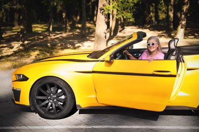 Photo of Stylish senior woman in sunglasses near modern cabriolet outdoors