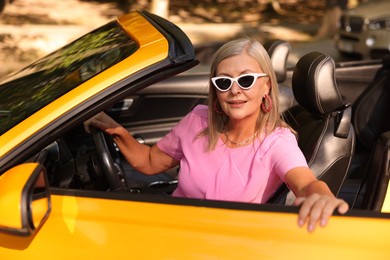 Photo of Stylish senior woman in sunglasses near modern cabriolet outdoors