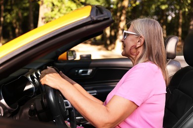 Photo of Stylish senior woman in sunglasses driving modern cabriolet outdoors