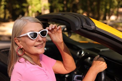 Photo of Stylish senior woman in sunglasses driving modern cabriolet outdoors