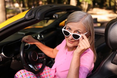 Photo of Stylish senior woman in sunglasses driving modern cabriolet outdoors