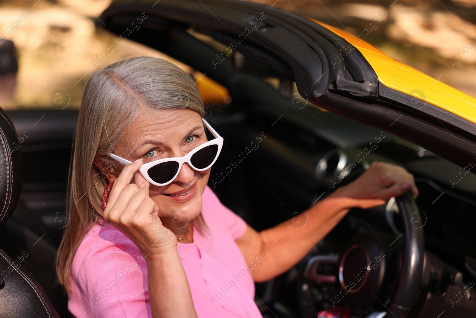 Photo of Stylish senior woman in sunglasses driving modern cabriolet outdoors