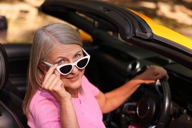 Photo of Stylish senior woman in sunglasses driving modern cabriolet outdoors