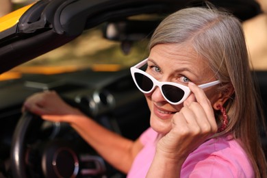 Photo of Stylish senior woman in sunglasses driving modern cabriolet outdoors