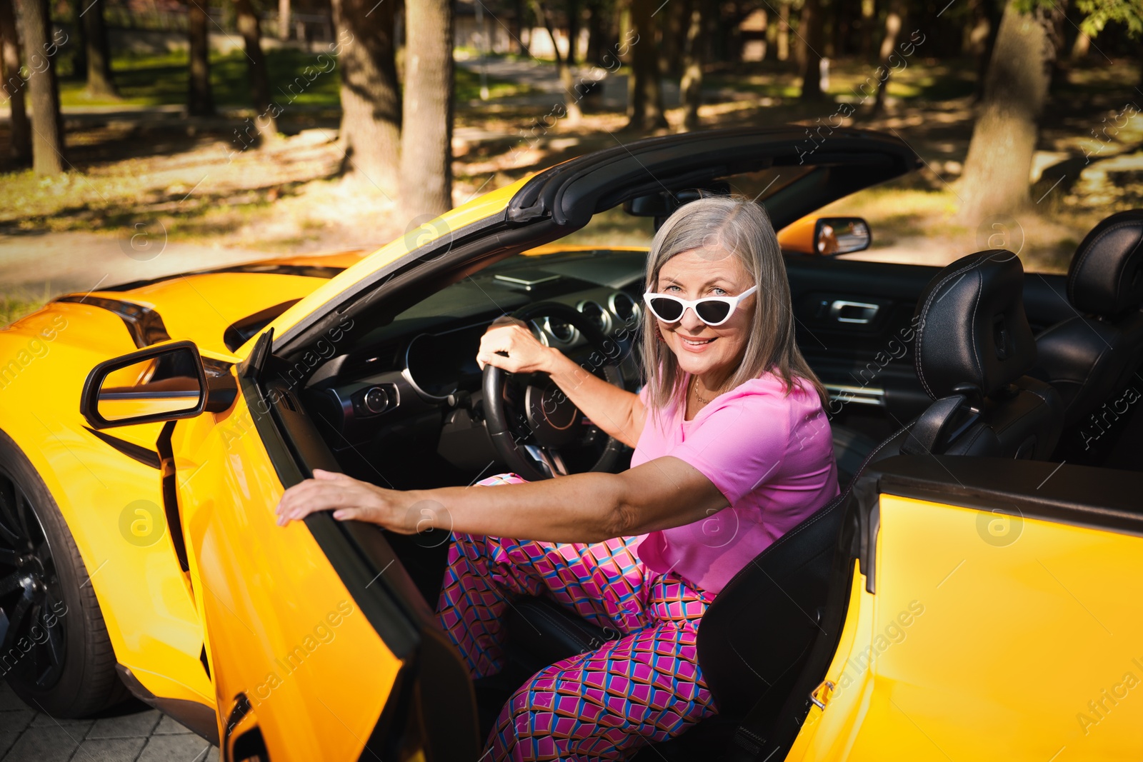 Stylish senior woman in sunglasses getting out of modern cabriolet outdoors Photo of Stylish senior woman in sunglasses getting out of modern cabriolet outdoors