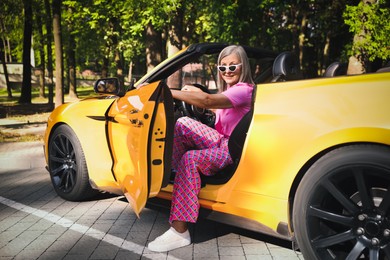 Photo of Stylish senior woman in sunglasses getting out of modern cabriolet outdoors