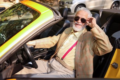 Photo of Stylish senior man in sunglasses driving modern cabriolet outdoors