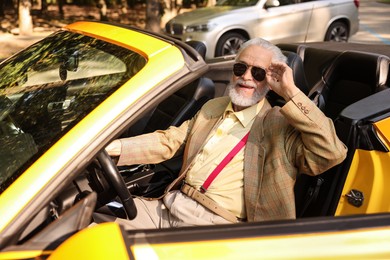 Photo of Stylish senior man in sunglasses driving modern cabriolet outdoors