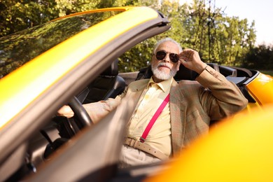 Photo of Stylish senior man in sunglasses driving modern cabriolet outdoors