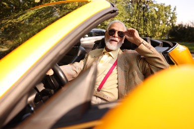 Photo of Stylish senior man in sunglasses driving modern cabriolet outdoors