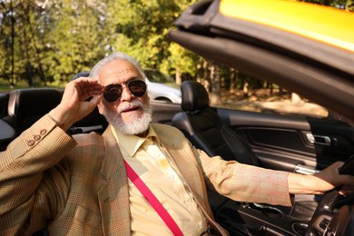 Photo of Stylish senior man in sunglasses driving modern cabriolet outdoors