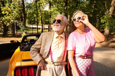 Photo of Stylish senior couple in sunglasses near modern cabriolet outdoors