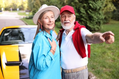 Photo of Stylish senior couple near modern cabriolet looking at something outdoors