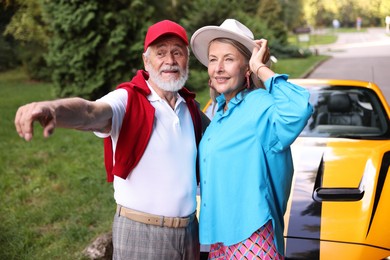 Photo of Stylish senior couple near modern cabriolet looking at something outdoors