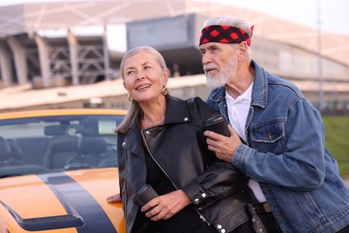 Photo of Stylish senior couple with takeaway coffee near modern cabriolet outdoors
