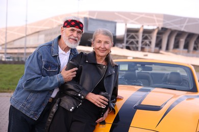 Photo of Stylish senior couple with takeaway coffee near modern cabriolet outdoors