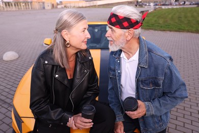 Photo of Stylish senior couple with takeaway coffee near modern cabriolet outdoors