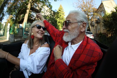 Photo of Senior couple enjoying cabriolet ride in city, wide angle lens