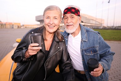 Photo of Stylish senior couple with takeaway coffee near modern cabriolet outdoors