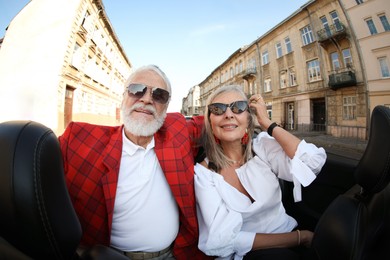 Photo of Senior couple enjoying cabriolet ride in city, wide angle lens