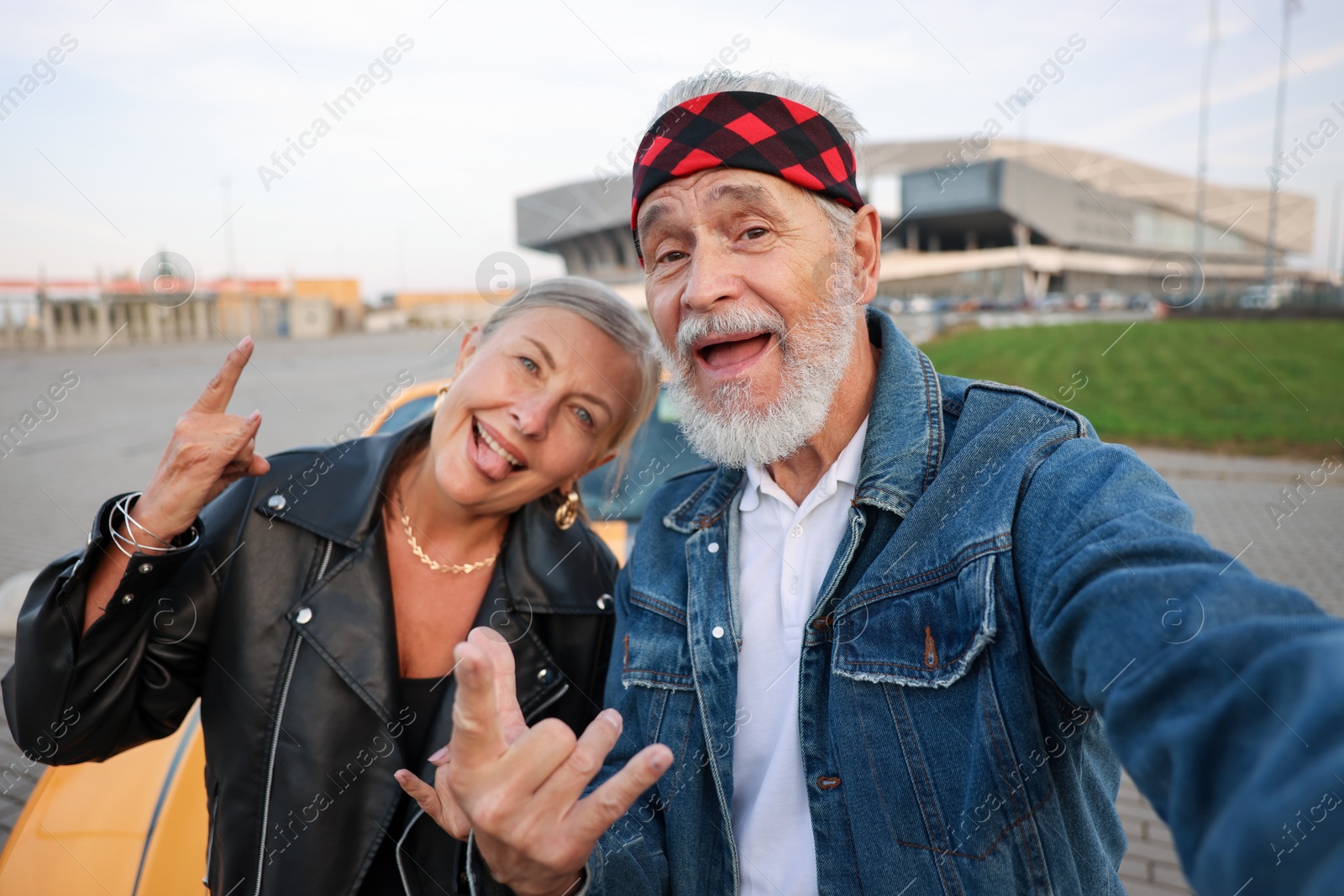 Stylish senior couple showing rock gesture while taking selfie near modern cabriolet outdoors Photo of Stylish senior couple showing rock gesture while taking selfie near modern cabriolet outdoors