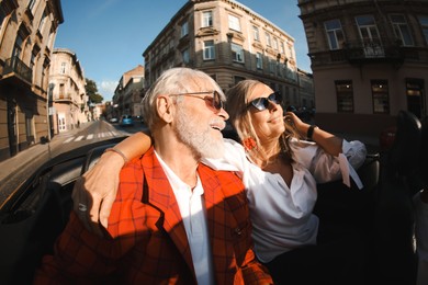 Photo of Senior couple enjoying cabriolet ride in city, wide angle lens
