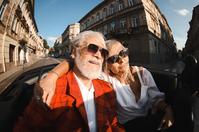 Photo of Senior couple enjoying cabriolet ride in city, wide angle lens