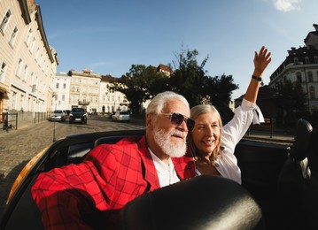 Photo of Senior couple enjoying cabriolet ride in city, wide angle lens