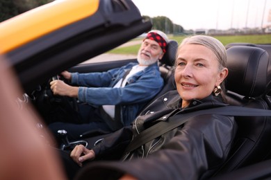 Photo of Senior woman taking selfie while man driving cabriolet outdoors, selective focus