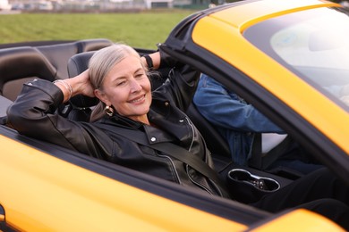 Photo of Stylish senior couple enjoying cabriolet ride outdoors, selective focus